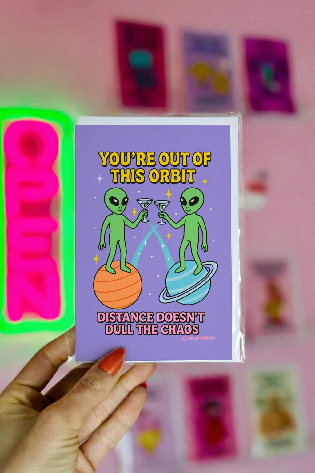 Two cartoon aliens clinking martini glasses while standing on planets with text “You’re out of this orbit — distance doesn’t dull the chaos.”