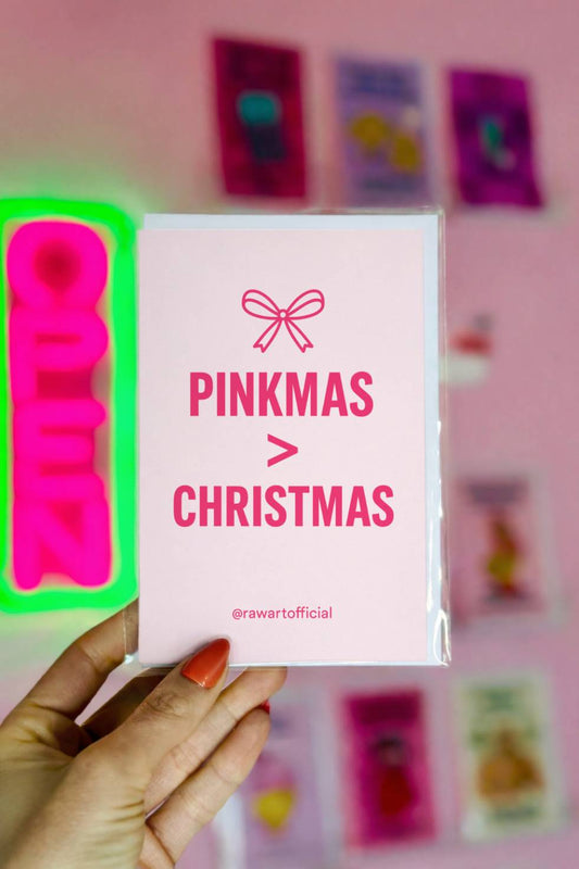 Funny Christmas card with pink text reading “Pinkmas > Christmas” on a minimal white background with bow illustration.