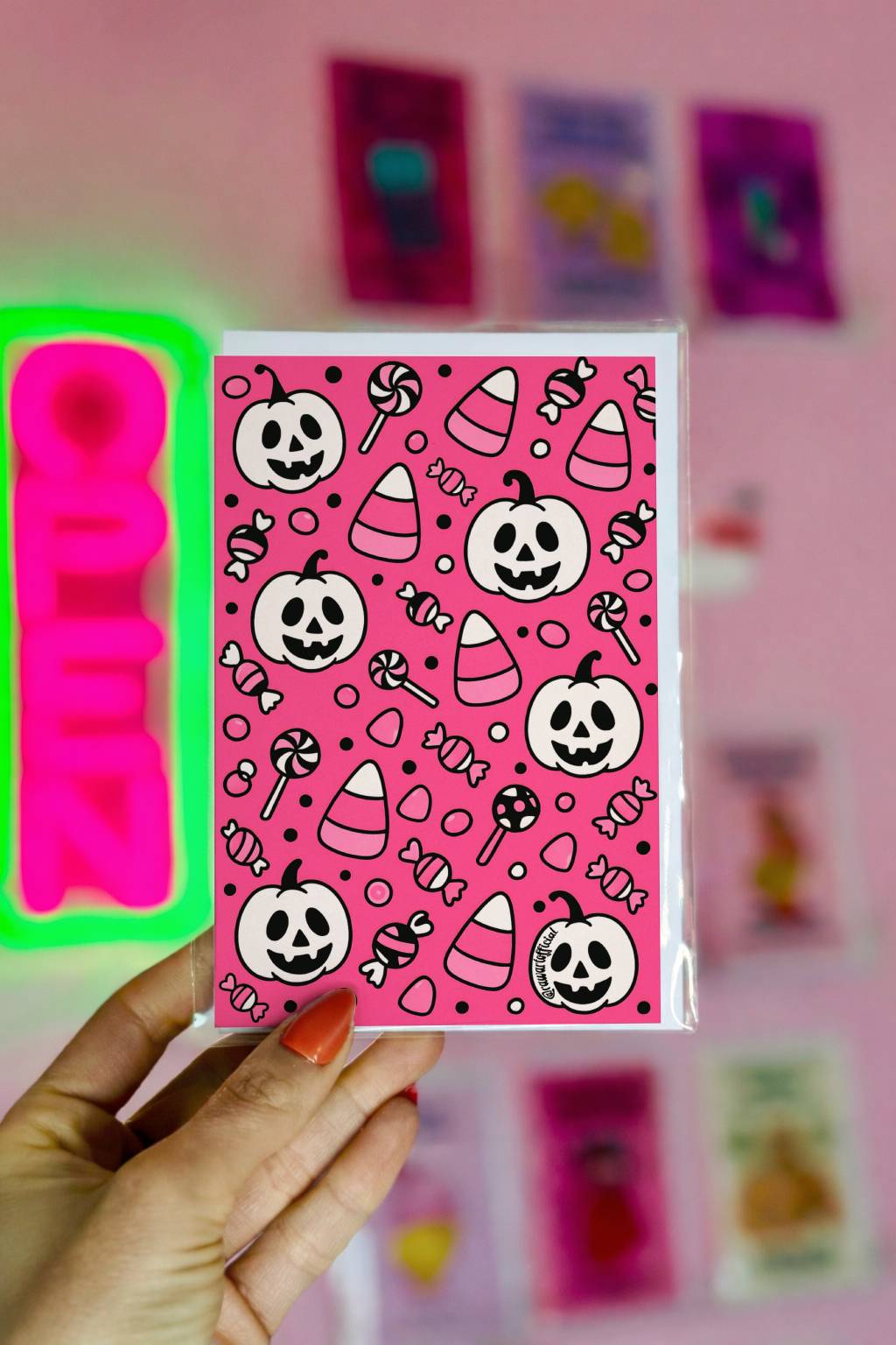 Greeting card featuring a retro pink Halloween pattern with smiling white pumpkins, candy corn, lollipops, and wrapped sweets in a cute cartoon style.