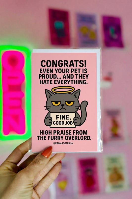 Card with a cartoon cat and humorous text held by a hand against a pink background with colorful cards.