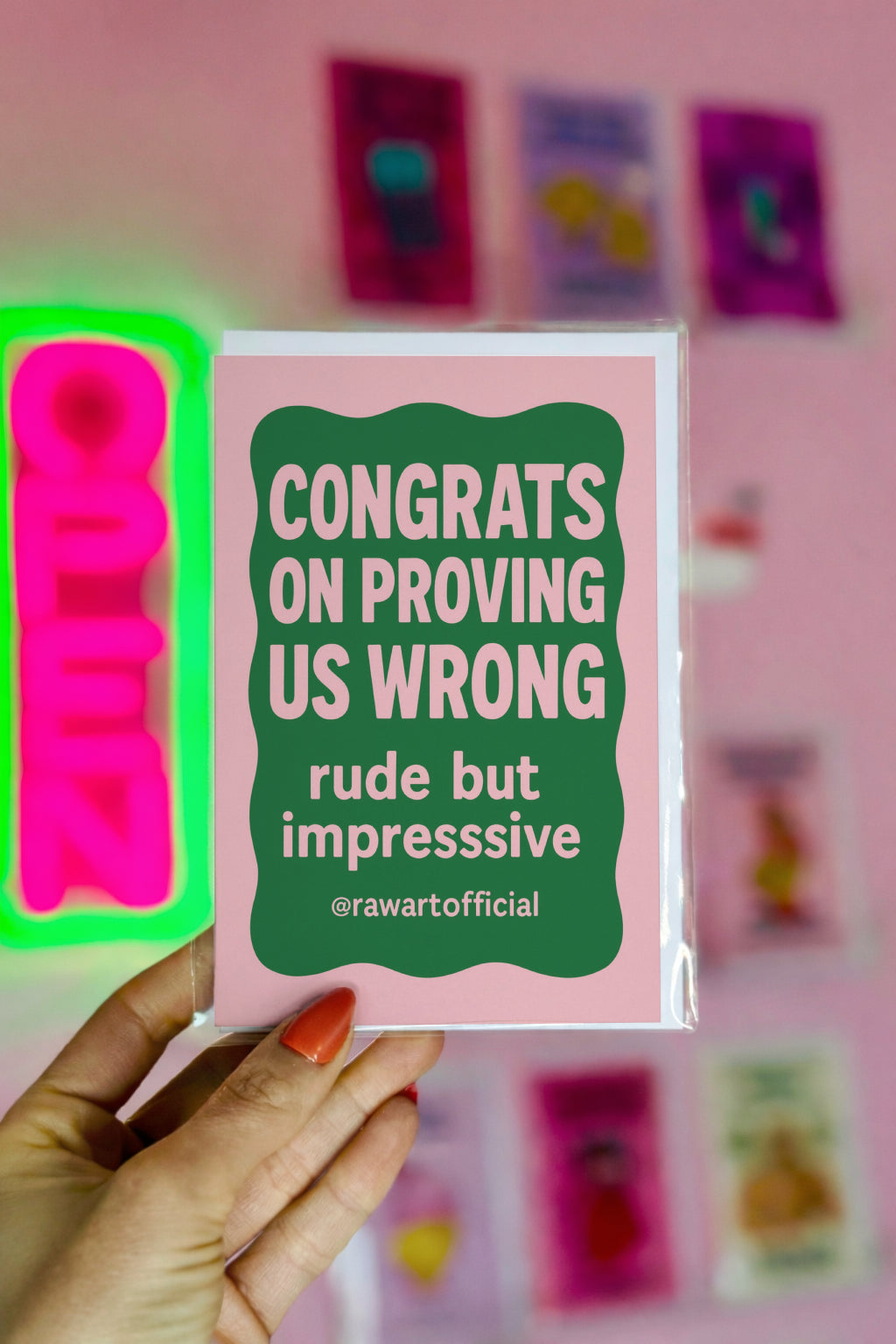A greeting card with a pink border and a green interior. The card reads "CONGRATS ON PROVING US WRONG rude but impresssive @rawartofficial". 