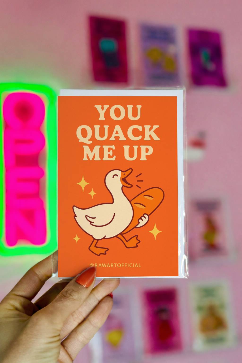 Bright orange greeting card with smiling duck holding baguette and text You Quack Me Up with @rawartofficial signature.
