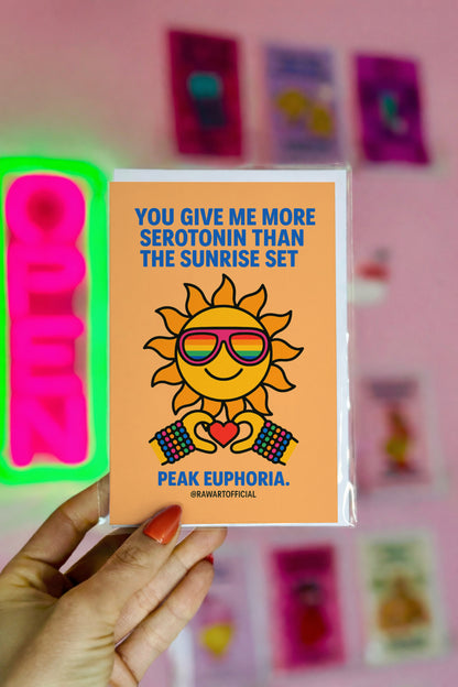 funny love card with smiling sun wearing rainbow sunglasses holding heart and text you give me more serotonin than the sunrise set