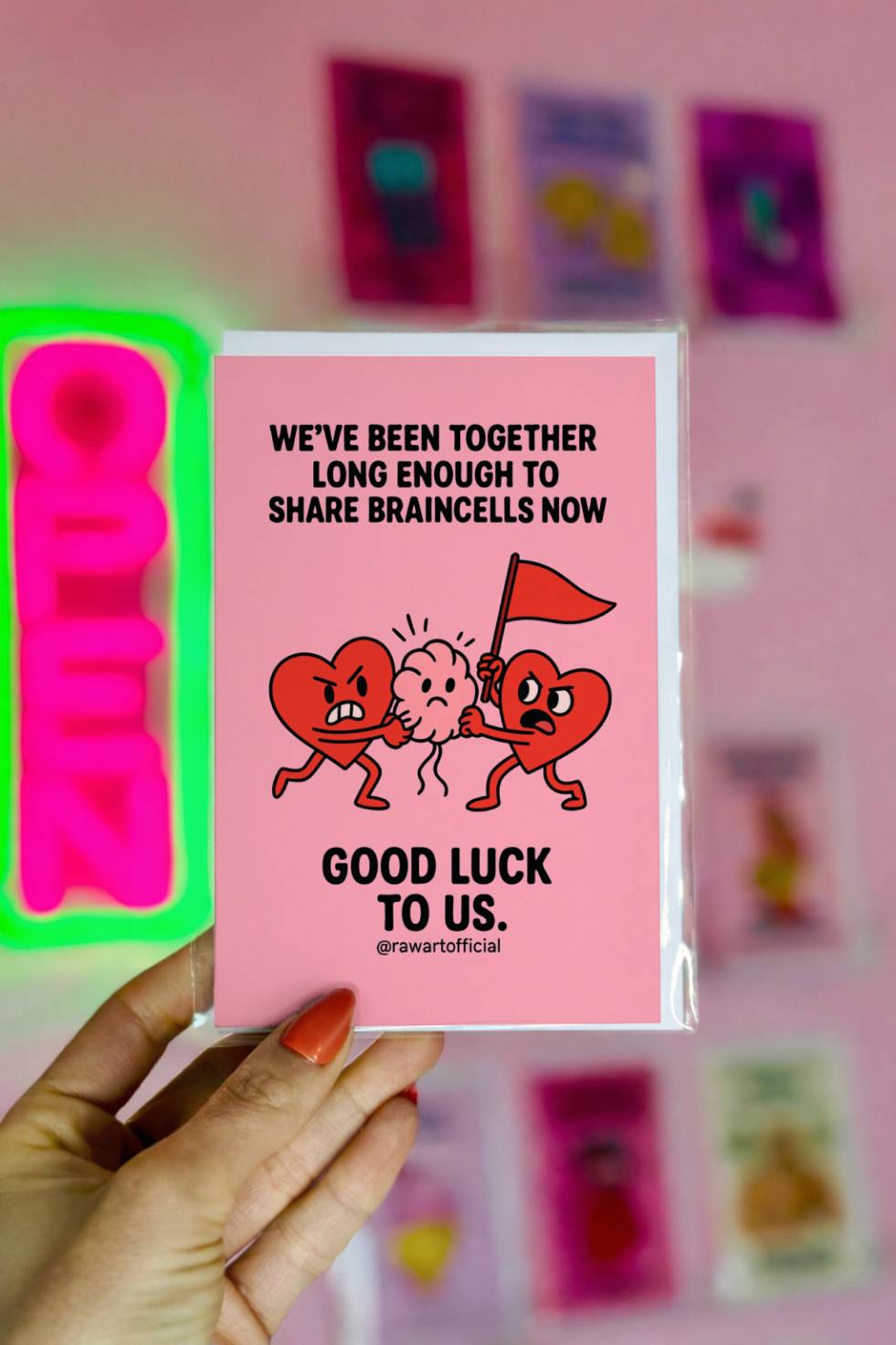 Funny greeting card reading “We’ve Been Together Long Enough to Share Braincells Now” with cartoon hearts fighting over a brain.