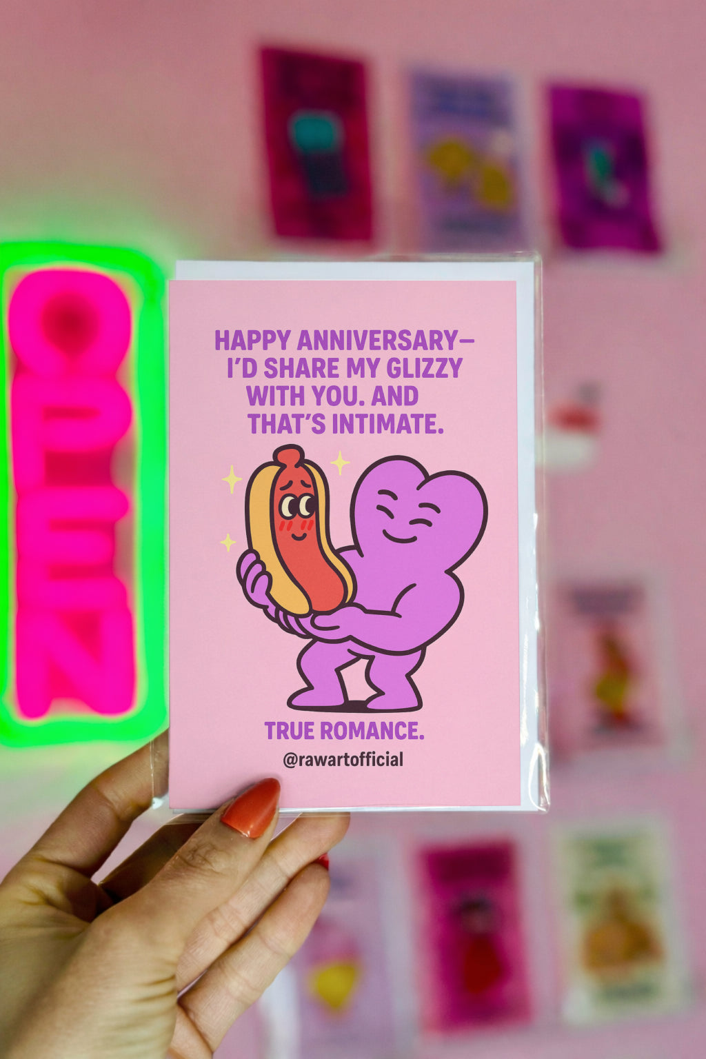 Illustration of a smiling purple heart character gently holding a blushing hot dog character, with romantic sparkles around them and anniversary text above.