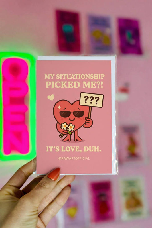Greeting card with heart holding flowers and sign reading “My Situationship Picked Me?!” on a pink background.