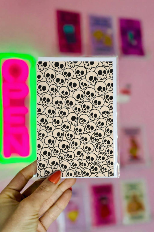 Pattern greeting card with cartoon skulls in bold black outlines on beige background, spooky-cute gothic stationery design.