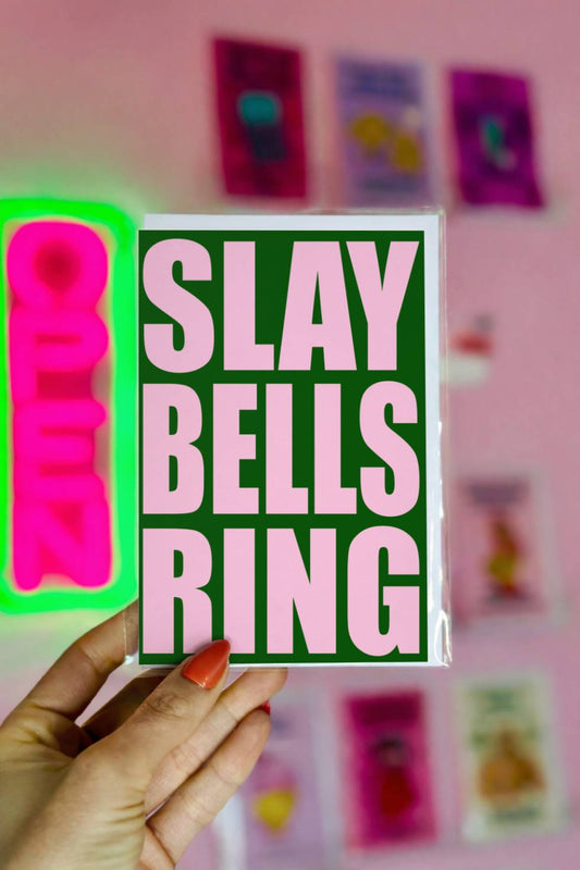 Funny Christmas greeting card with bold pink text reading “Slay Bells Ring” on a dark green background in retro typography.