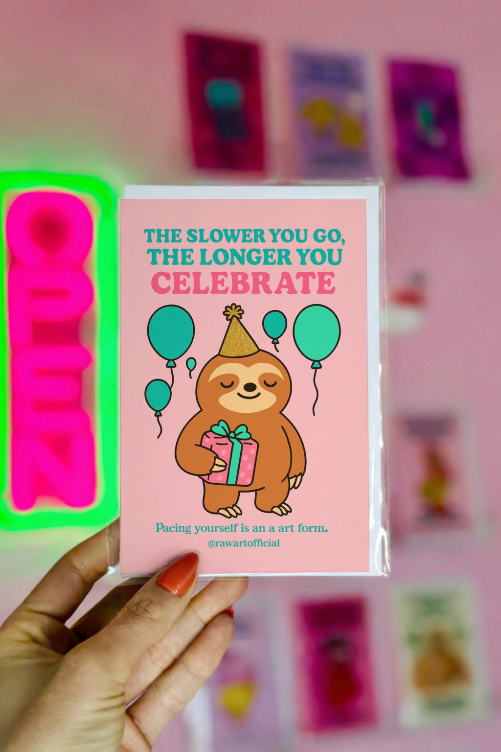 Pink birthday card featuring smiling sloth in party hat holding gift with balloons and text about celebrating longer.