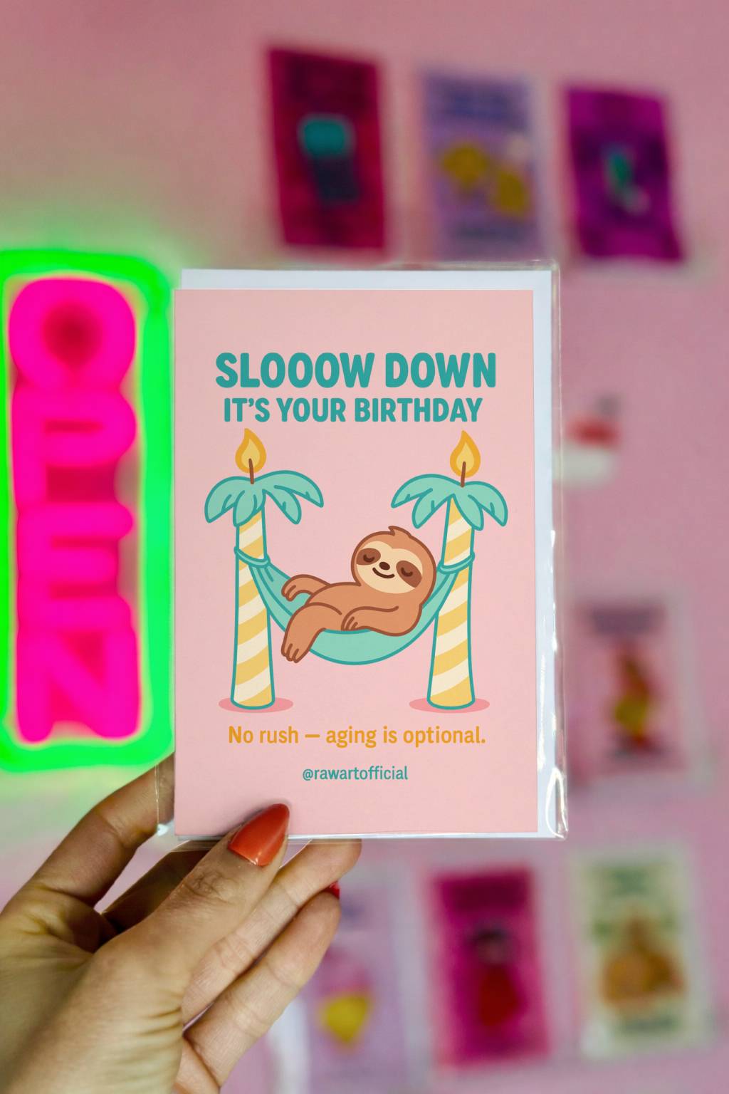 Pink birthday card featuring sloth in hammock between candle palm trees with text “Slooow Down It’s Your Birthday.”