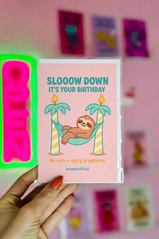 Pink birthday card featuring sloth in hammock between candle palm trees with text “Slooow Down It’s Your Birthday.”