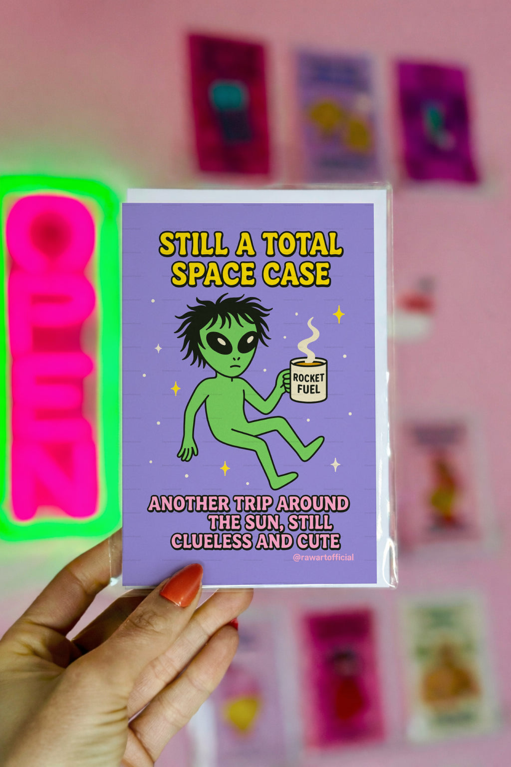Green alien holding a coffee mug labeled “Rocket Fuel” floating in space with text “Still a Total Space Case.”