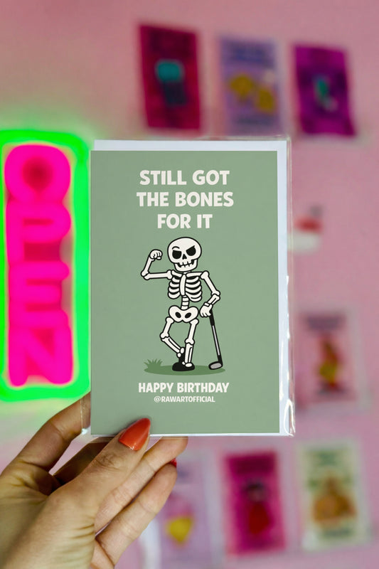 Funny golf birthday card showing a flexing cartoon skeleton holding a golf club with the words “Still Got the Bones for It” and “Happy Birthday” on a green background.
