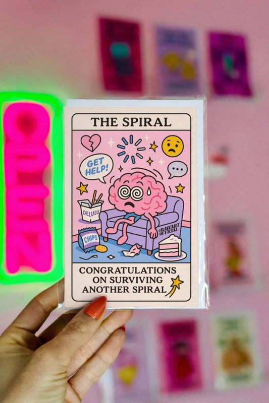 Funny tarot-style birthday card titled “The Spiral” with a frazzled brain character on a couch surrounded by snacks and text “Congratulations on Surviving Another Spiral.”