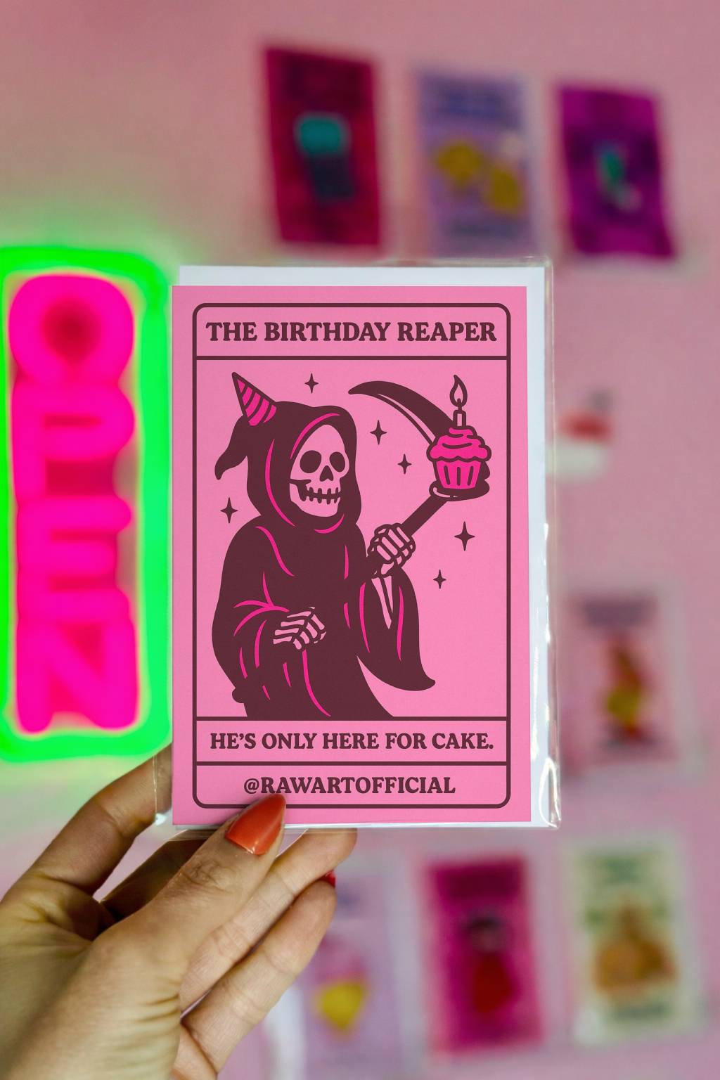 Pink gothic birthday card featuring the Grim Reaper holding a scythe with a cupcake, captioned “He’s only here for cake.”