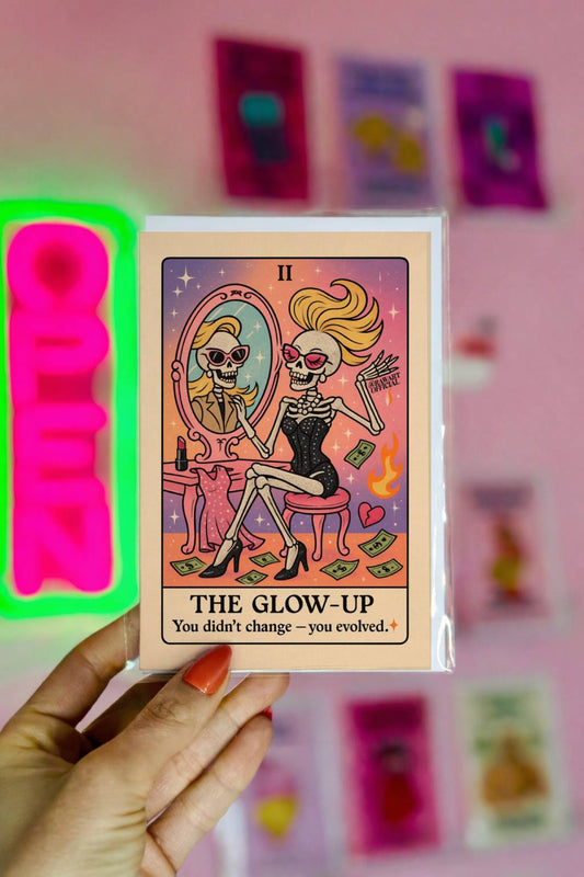 Tarot-style greeting card featuring a glamorous skeleton in a black dress at a vanity mirror with cash flying and the text “The Glow-Up – You didn’t change, you evolved.”