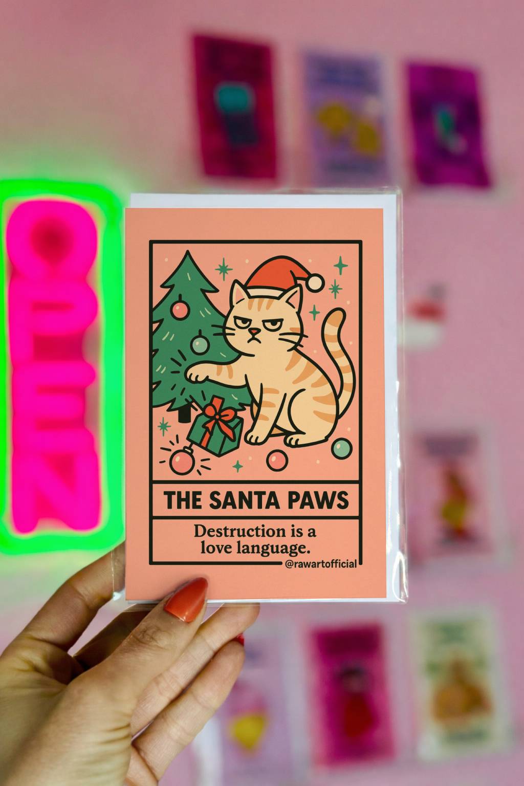 Funny tarot-style Christmas card featuring a cat in a Santa hat knocking ornaments off a tree with text “The Santa Paws destruction is a love language”