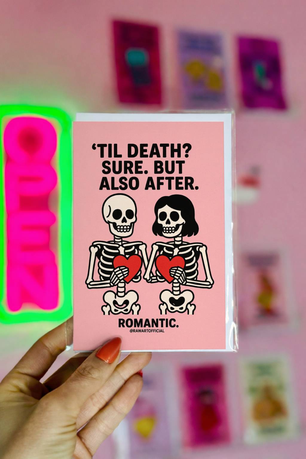Cute skeleton couple holding hearts on a pink background with text “’Til death? Sure. But also after.” Romantic spooky valentine card.