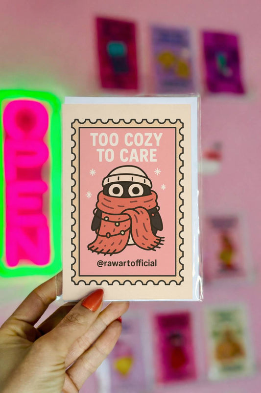 Minimalist Christmas card featuring a bundled-up penguin in scarf and hat with text “Too Cozy To Care” in a soft retro style