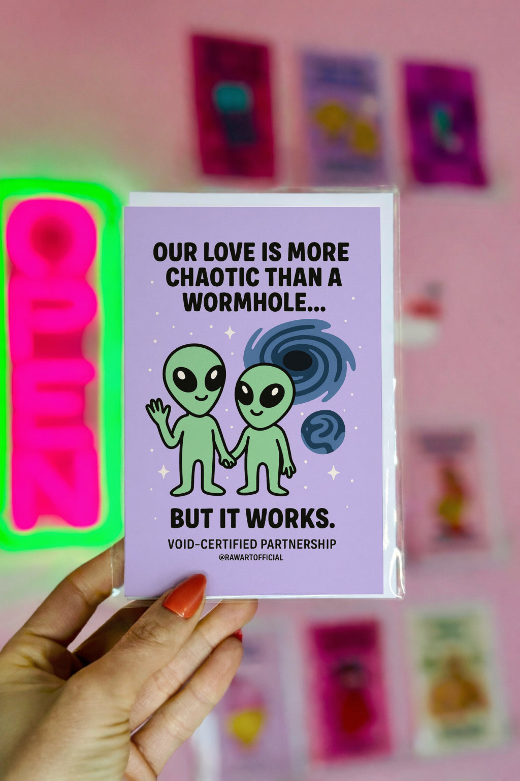 Greeting card with a purple background featuring two green alien figures and the text "OUR LOVE IS MORE CHAOTIC THAN A WORMHOLE... BUT IT WORKS." 
